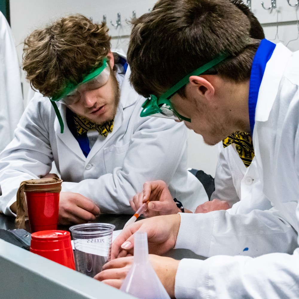 Students wearing safety goggles work together during a lab event.